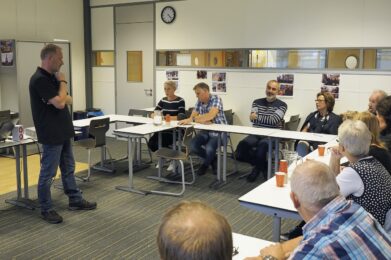 Deelnemers zitten aan een tafel en luisteren interactief naar de docent