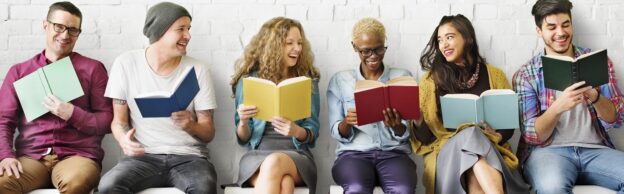 Meerdere personen zitten naast elkaar met een boek, leren samen en lachen naar elkaar.